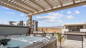 A hot tub under a pergola with a view of modern buildings and a desert landscape. - Beech Bungalow: Desert Color Lagoon + Beaches,  Hot Tub (St. George)