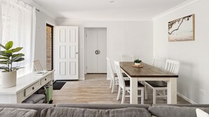 A modern living room with a wooden dining table, white chairs, a grey sofa, and a potted plant. - Pets welcome, family friendly home. 5 minute drive to beaches. (Aroona)