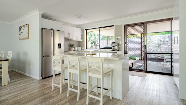 A modern kitchen with a central island, bar stools, a refrigerator, and a sliding glass door leading to an outdoor area. - Pets welcome, family friendly home. 5 minute drive to beaches. (Aroona)