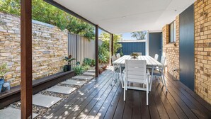 An outdoor patio with a wooden deck, a white table with chairs, and a stone wall. - Pets welcome, family friendly home. 5 minute drive to beaches. (Aroona)