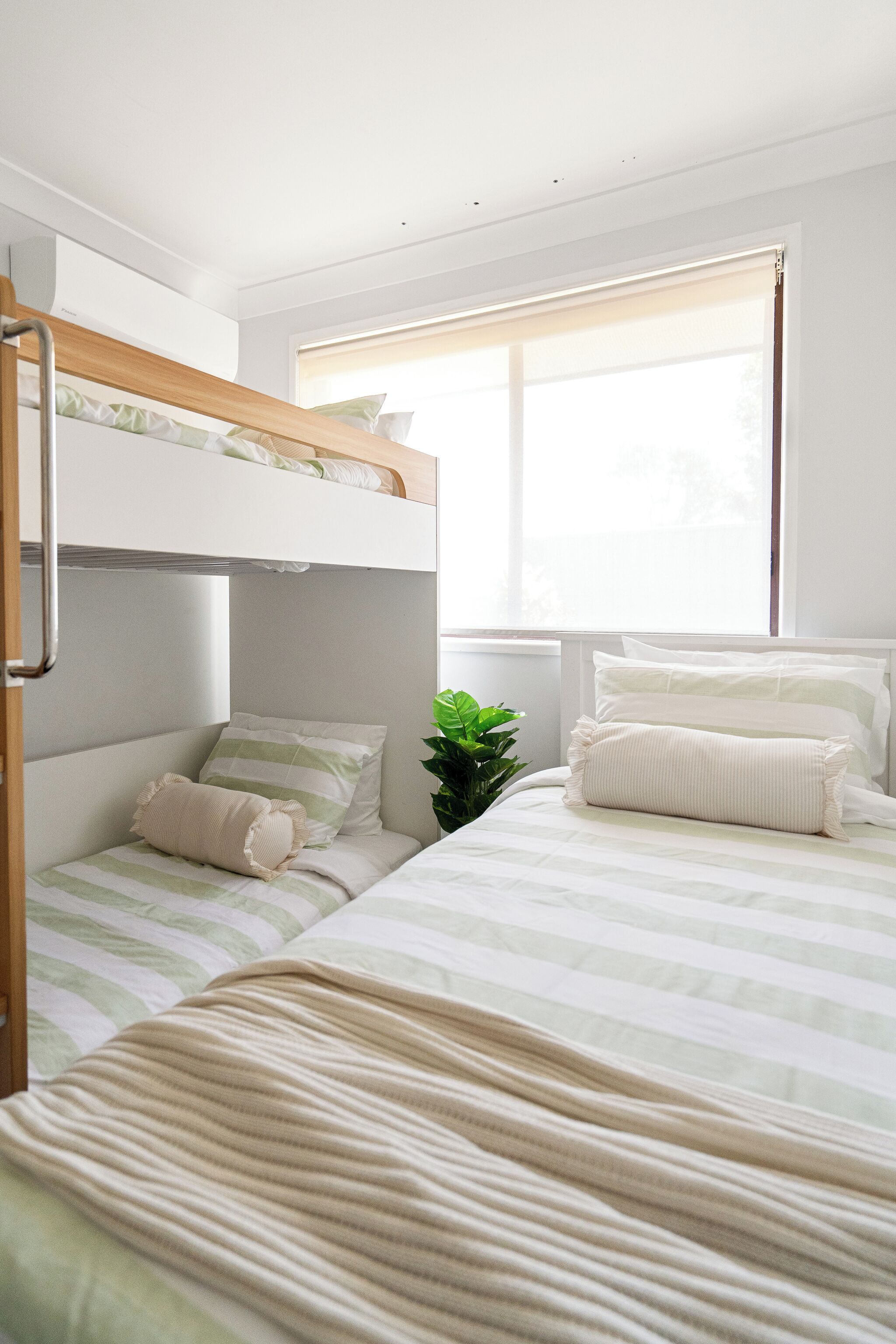 Dormitorio con literas, ventana, planta en maceta y radiador.
