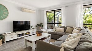 A living room with a television, sofa, coffee table, and large windows. - Pets welcome, family friendly home. 5 minute drive to beaches. (Aroona)