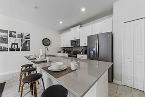 Una cocina moderna con armarios blancos, una isla central con taburetes, un refrigerador y un microondas.