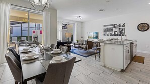A modern kitchen with a central island, dining area with a table set for four, and a living space with a sofa and coffee table. - Themed Home w/ Pool, Resort Perks & Prime Location (Kissimmee)