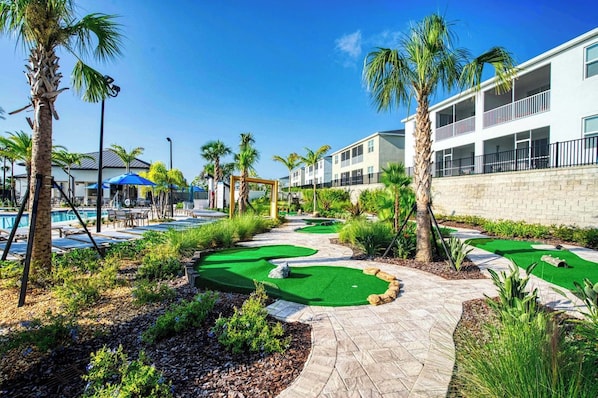 Campo de golf con zona de piscina, palmeras y un edificio con balcones.