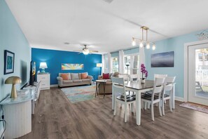 Relax in this open-plan living space with a large window, ceiling fan, and modern chandelier.