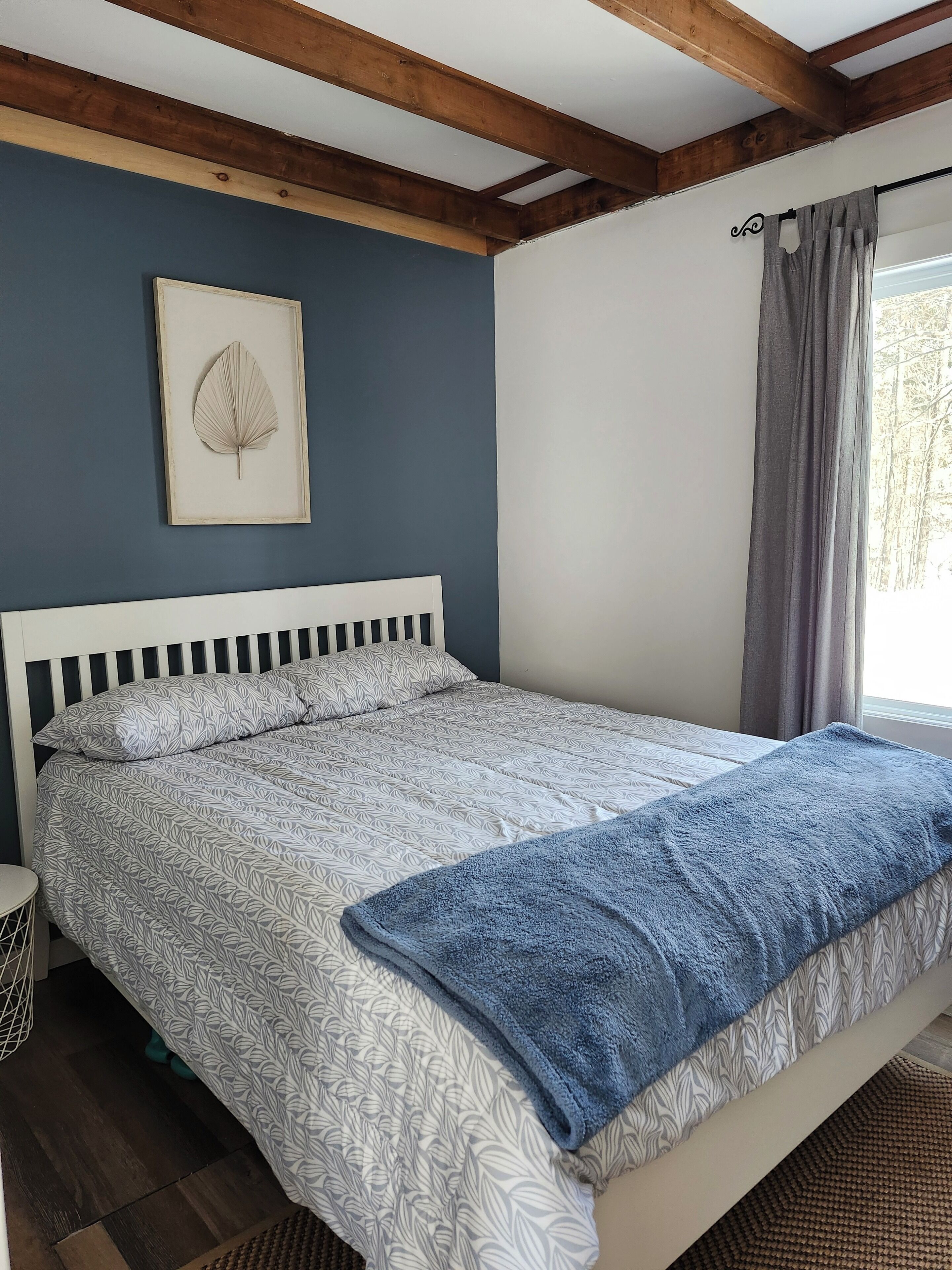 Ein Schlafzimmer mit einem Bett, einem Kopfteil, einer Wanddekoration mit Blattformen und einem Fenster mit Vorhängen.
