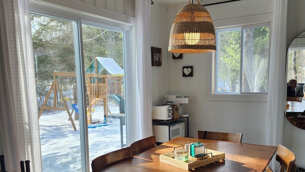 Un tavolo da pranzo in legno con sedie, una lampada di vimini appesa e vista su un'area esterna con un pavimento in legno.