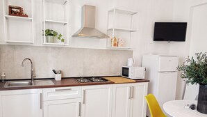 A modern kitchen with white cabinets, a stainless steel sink, a microwave, and a gas stove. There is a yellow chair and a small table with a plant. - Spacious apartment in historic country residence, between Perugia and Assisi (Perugia)