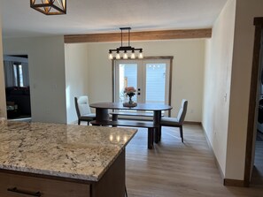 A modern kitchen with a granite countertop, wooden beams, and a dining area with a table and chairs.
