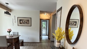 A modern interior with a dining area, a black console table with a mirror, and a hallway leading to a door.