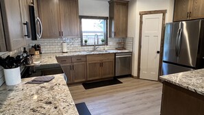 A modern kitchen with wooden cabinets, a stainless steel refrigerator, and a granite countertop.