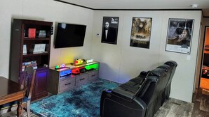En stue med fjernsyn, reol, spillekonsol, lædersofa og filmplakater på væggen.