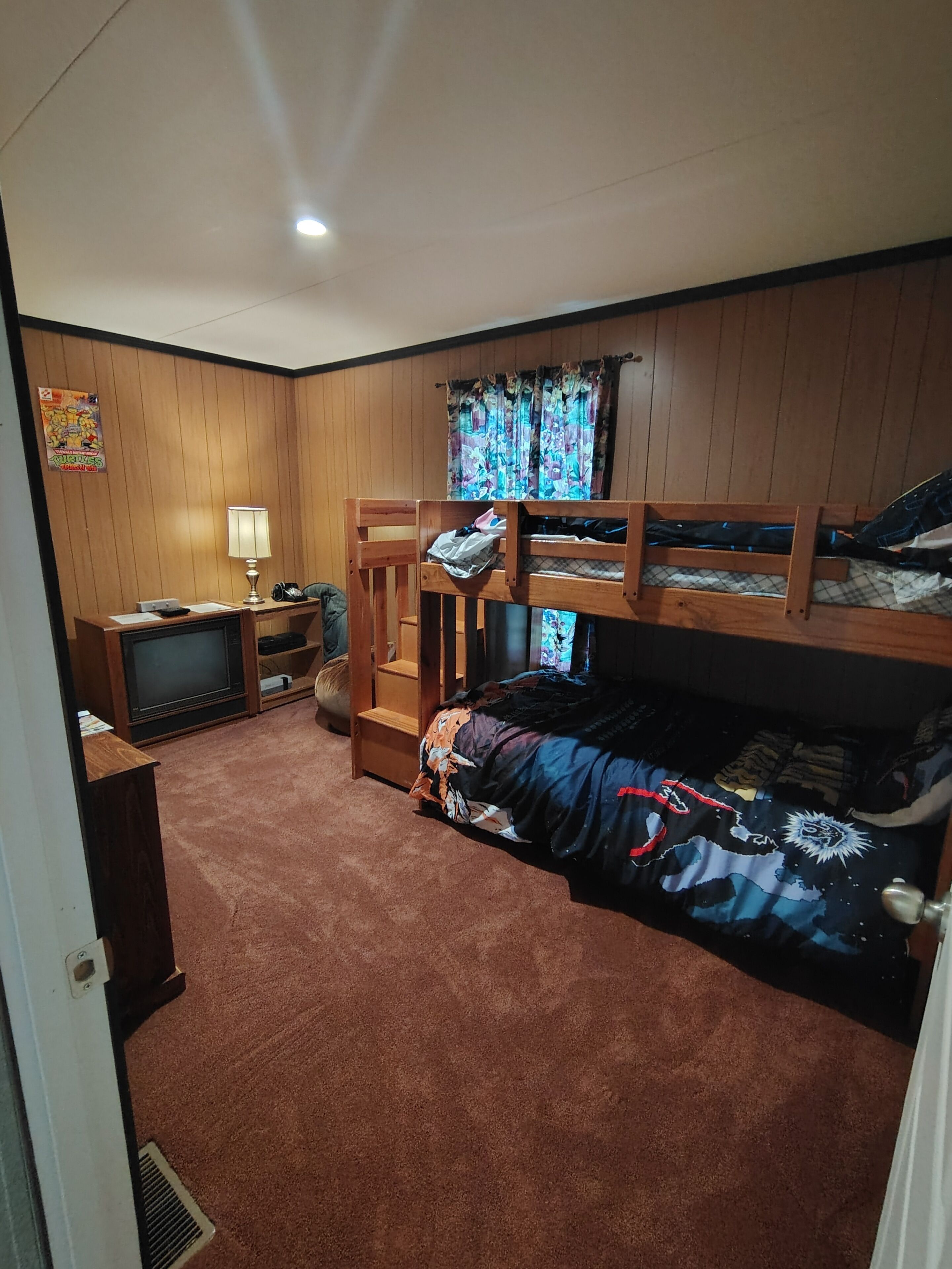 A bedroom with bunk beds, a television, a desk with a lamp, and a poster on the wall.