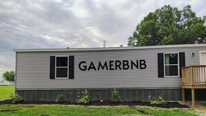 En autocamper med navnet 'GAMERBNB' på siden, en lille terrasse og et græsstykke foran.