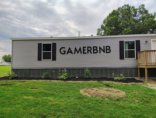 A mobile home with the name 'GAMERBNB' on the side, a small deck, and a grassy area in front.
