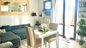 Una sala de estar con sofá, una mesa de comedor con sillas, un radiador y una ventana con cortinas.