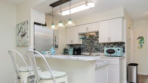 A kitchen with white cabinets, a marble countertop, a refrigerator, a sink, and a trash can. - Pet Friendly 1 BR Condo with a View! (Carolina Beach)