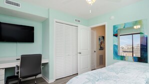 A bedroom with a bed, a desk with a chair, a TV, a closet, and a painting on the wall. - Pet Friendly 1 BR Condo with a View! (Carolina Beach)