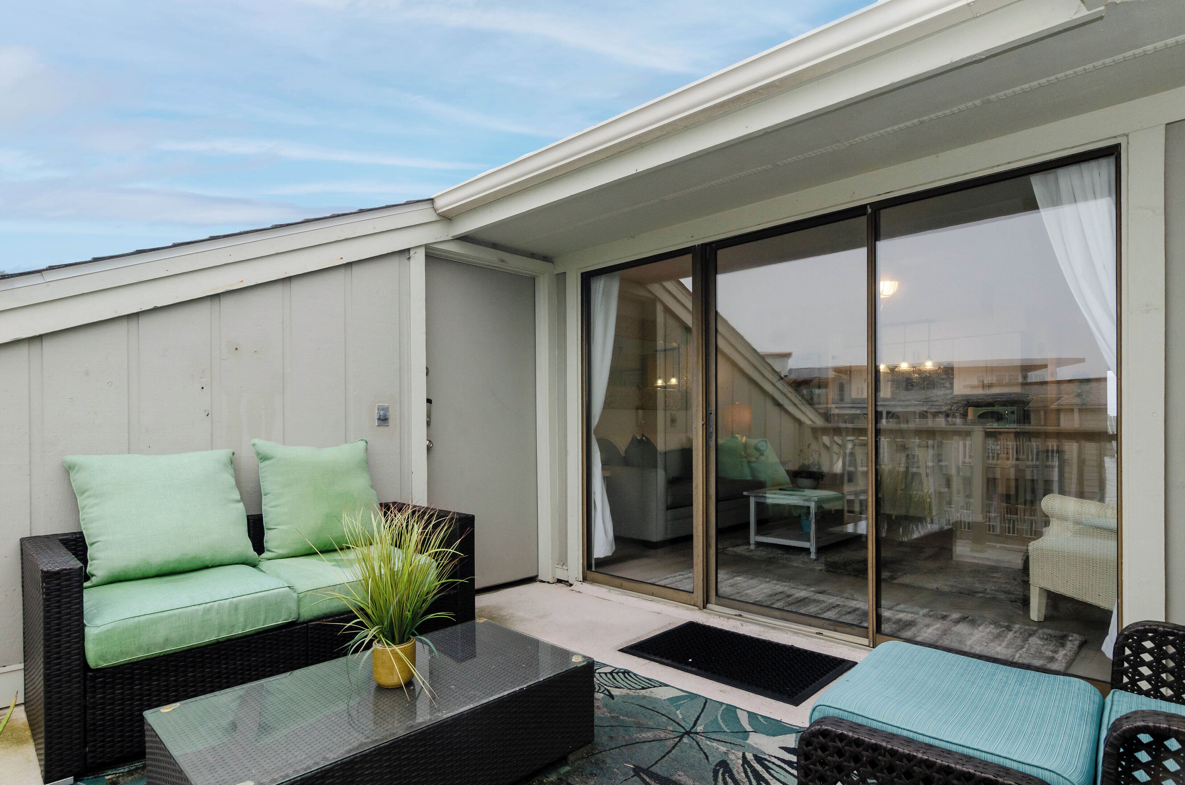 Een balkon met een rieten bank, een glazen tafel en een bloempot.