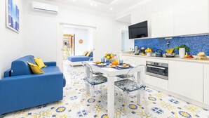 A modern living room with a blue sofa and a dining area with a white table and chairs. - Marescala Vacation - Casa Cicirusso, elegant apartment in Sorrento town center (Sorrento)