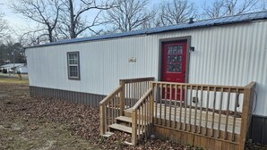 A small, single-story metal building with a red door and a wooden staircase leading to a deck.