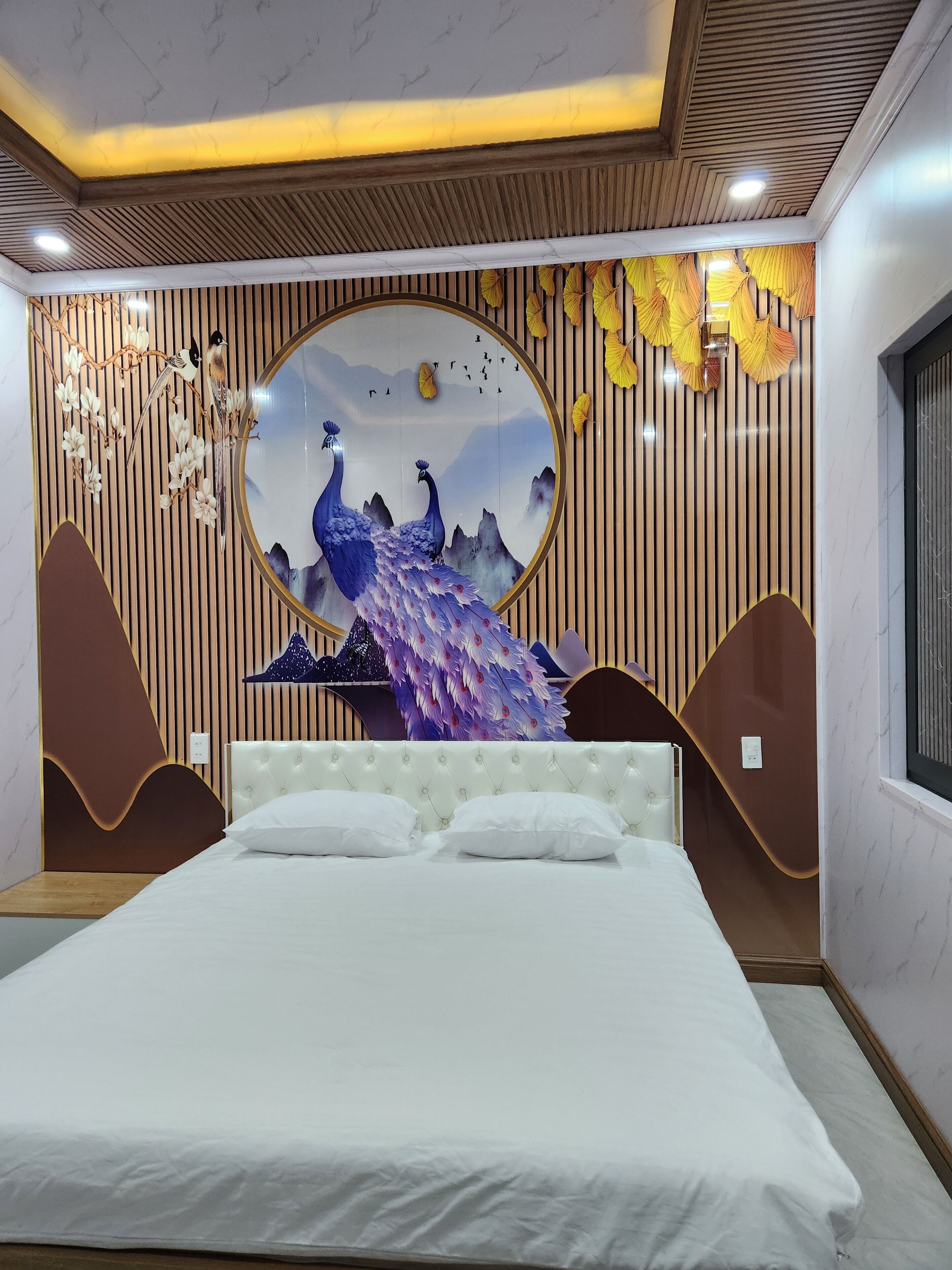 Ein Schlafzimmer mit einem großen Bett, einer Wandmalerei mit Pfauen und einer Holzbalkendecke.