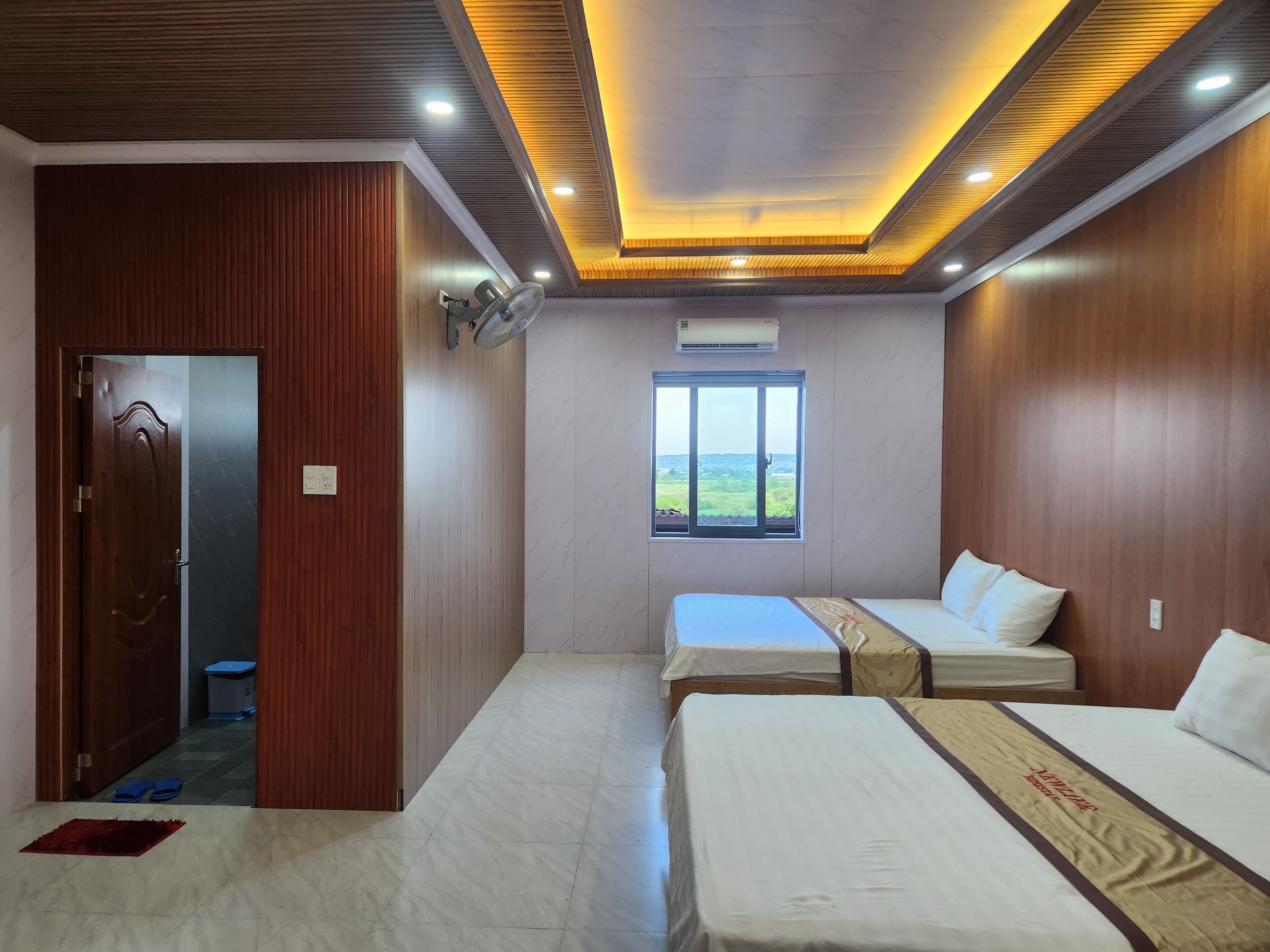A hotel room with two beds, a window with a view, wooden paneling, and a ceiling with recessed lighting.