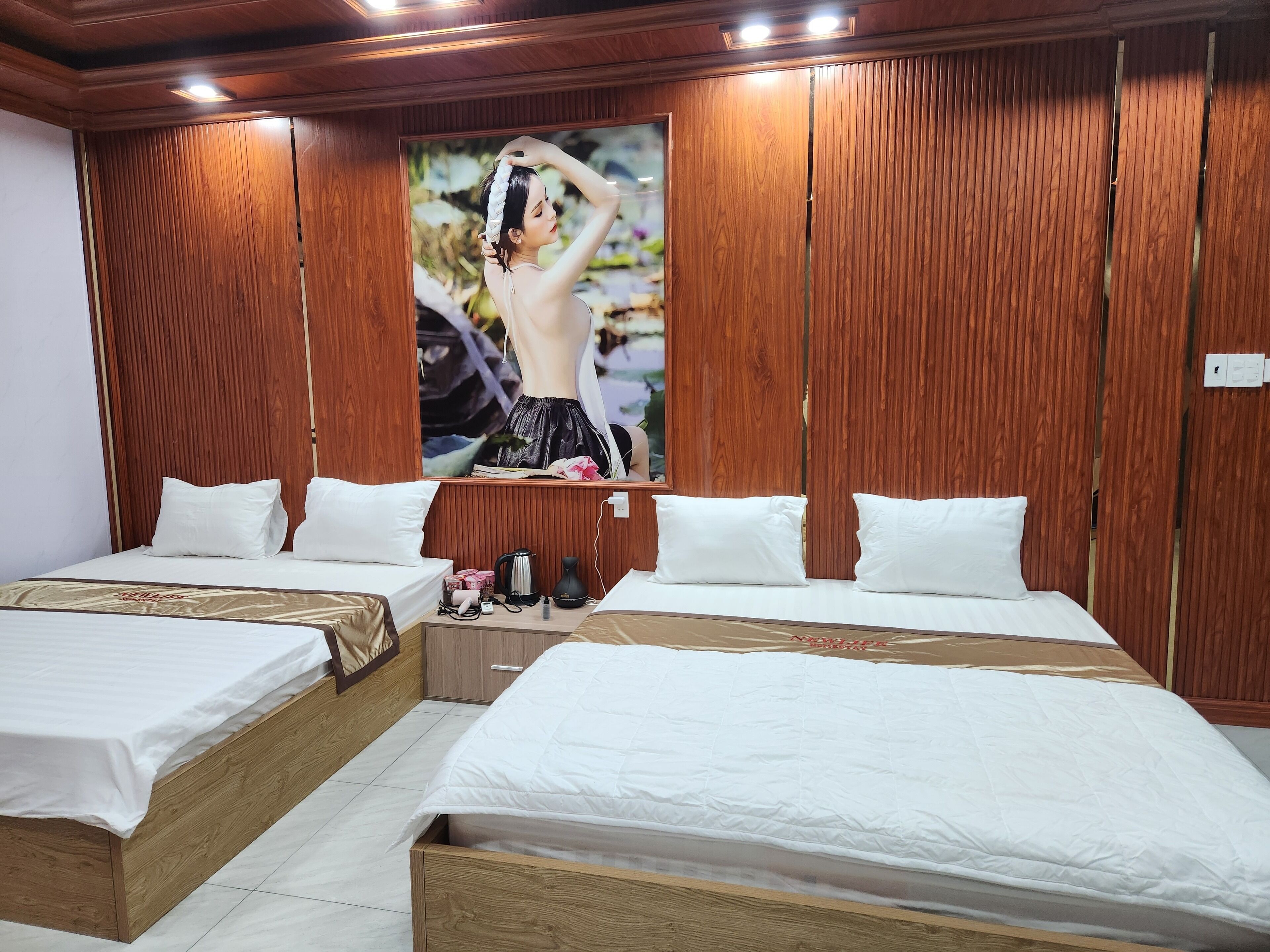 A hotel room with two beds, wooden paneling on the walls, a large mirror, and a nightstand with a lamp and a coffee maker.