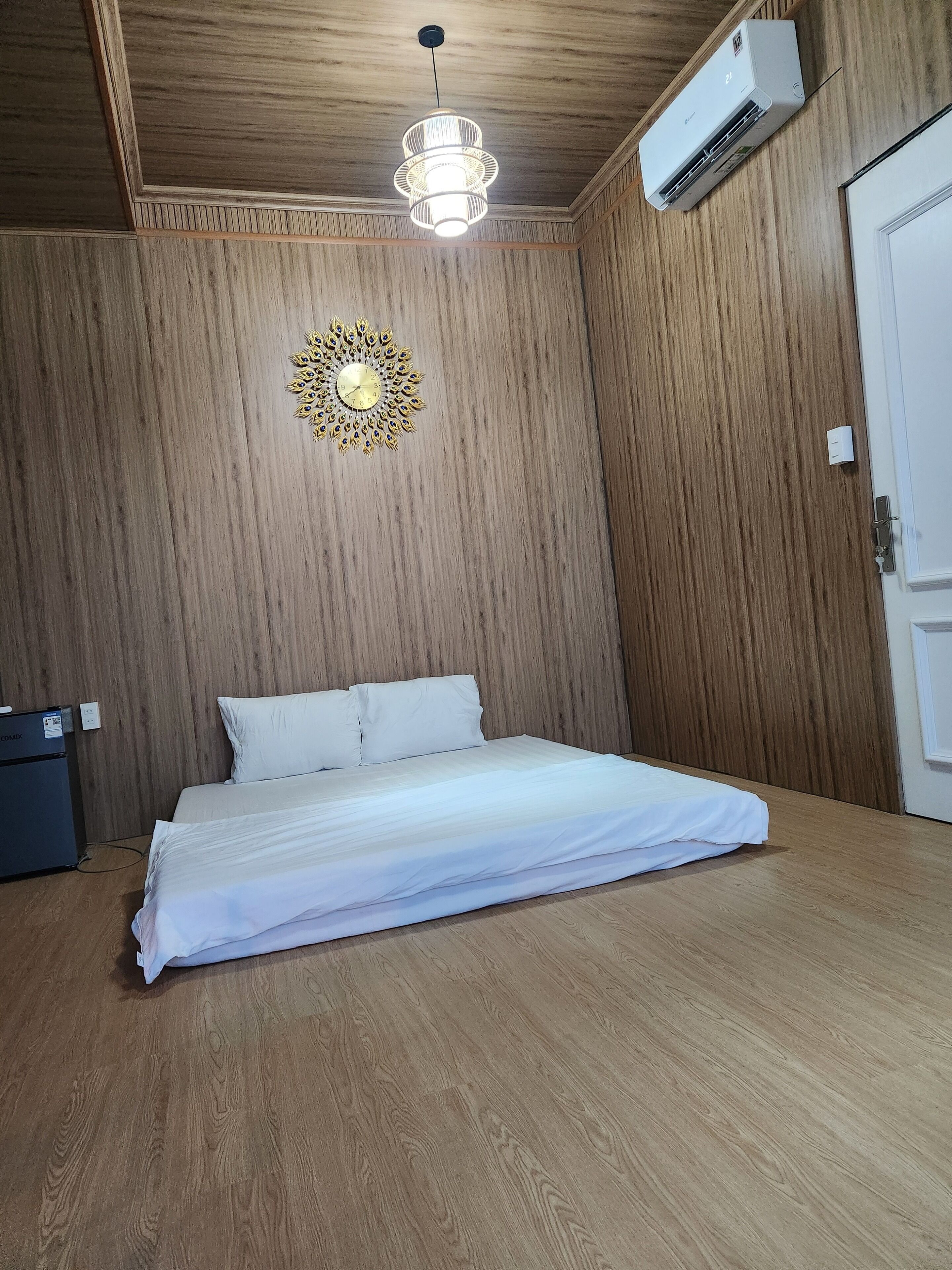 A bedroom with a wooden ceiling, a decorative wall hanging, a bed with white bedding, and an air conditioning unit mounted on the wall.