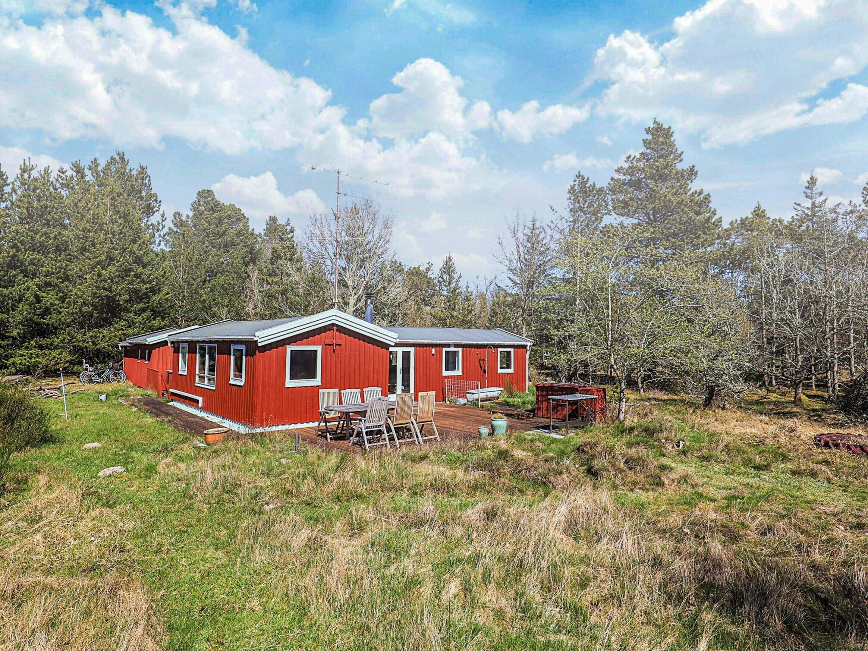 A red cabin with a deck, surrounded by trees and grass.