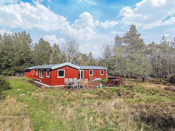 A red cabin with a deck, surrounded by trees and grass.