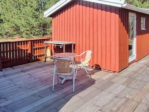 A red wooden structure with a glass door, a small table, and two chairs on a wooden deck.