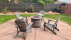 A patio with Adirondack chairs, a stone fire pit, and a metal table. - Scenic Escape in Kanab | Pet-Friendly | Community Pool & Hot Tub (Kanab)