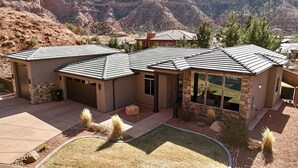 A modern house with a stone facade, multiple garage doors, and a large window overlooking a mountainous landscape. - Scenic Escape in Kanab | Pet-Friendly | Community Pool & Hot Tub (Kanab)