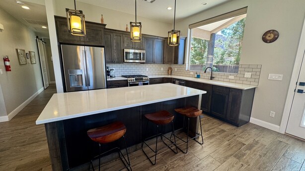 A modern kitchen with a large island, dark cabinetry, stainless steel appliances, and pendant lighting. - Scenic Escape in Kanab | Pet-Friendly | Community Pool & Hot Tub (Kanab)
