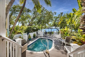 A pool area with a white fence, lounge chairs, and potted plants.