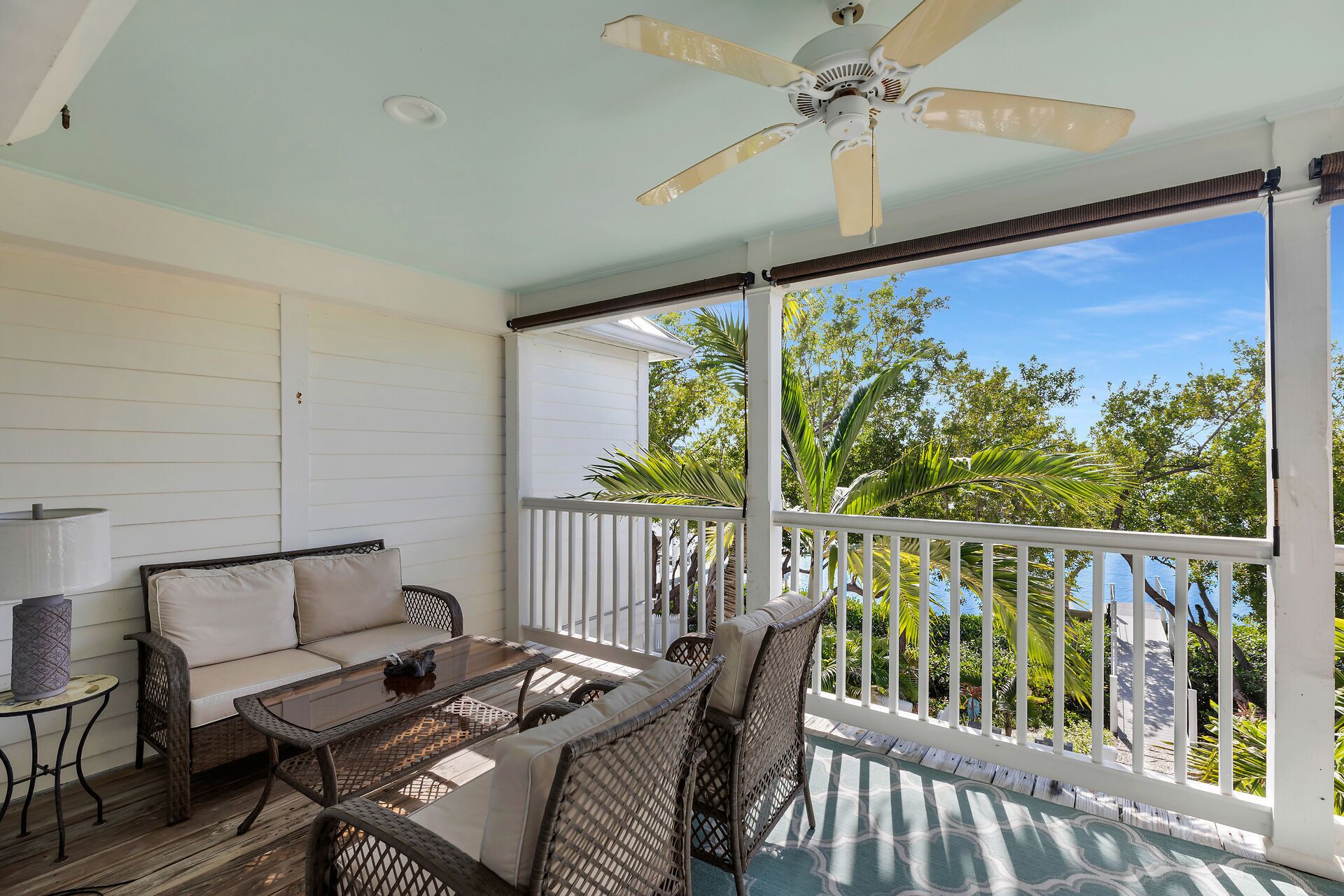 A covered outdoor seating area with wicker furniture, a ceiling fan, and a view of the outdoors.