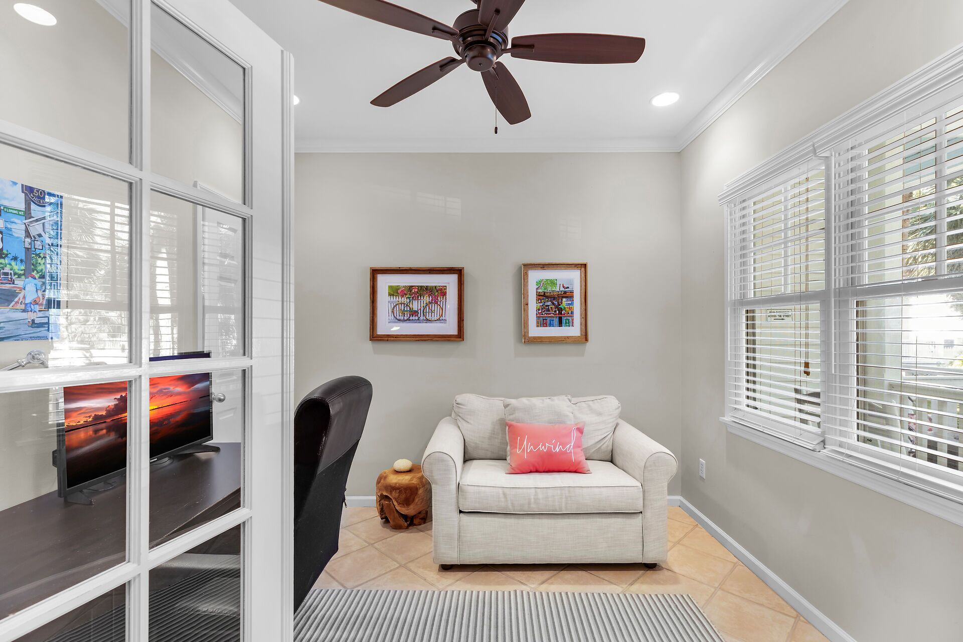 A living room with a ceiling fan, a sofa with a cushion, a small stool, and two framed pictures on the wall.
