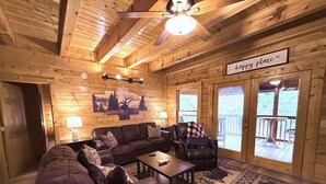 L’intérieur chaleureux d’un chalet avec un plafond en bois, un canapé en cuir, un fauteuil inclinable, une table basse et un tapis.