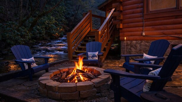 Une cabane en rondins avec une cheminée en pierre, une terrasse en bois et un espace salon extérieur.