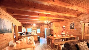 L’intérieur chaleureux d’un chalet comprend une table à manger en bois, préparée pour le petit-déjeuner, un canapé et un coin cuisine équipé d’un réfrigérateur et d’une cuisinière.