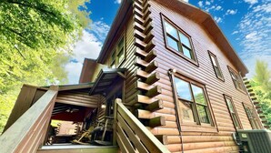 Une cabane en rondins avec un escalier menant à l’entrée, entourée d’arbres.