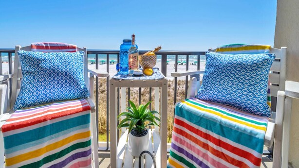 Dos sillones a rayas con cojines estampados, una mesita con una botella, un cuenco y una planta, con vista a la playa.