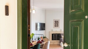 A green door with a keypad lock, a dining area with a table set for four, a television mounted on the wall, and a fireplace.