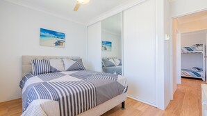 A bedroom with a bed, a large mirror, and a view of a beach through the window. - Amanda Court 14, 1-5 Weatherly Close - 250 metres from Shoal Bay Beach (Nelson Bay)