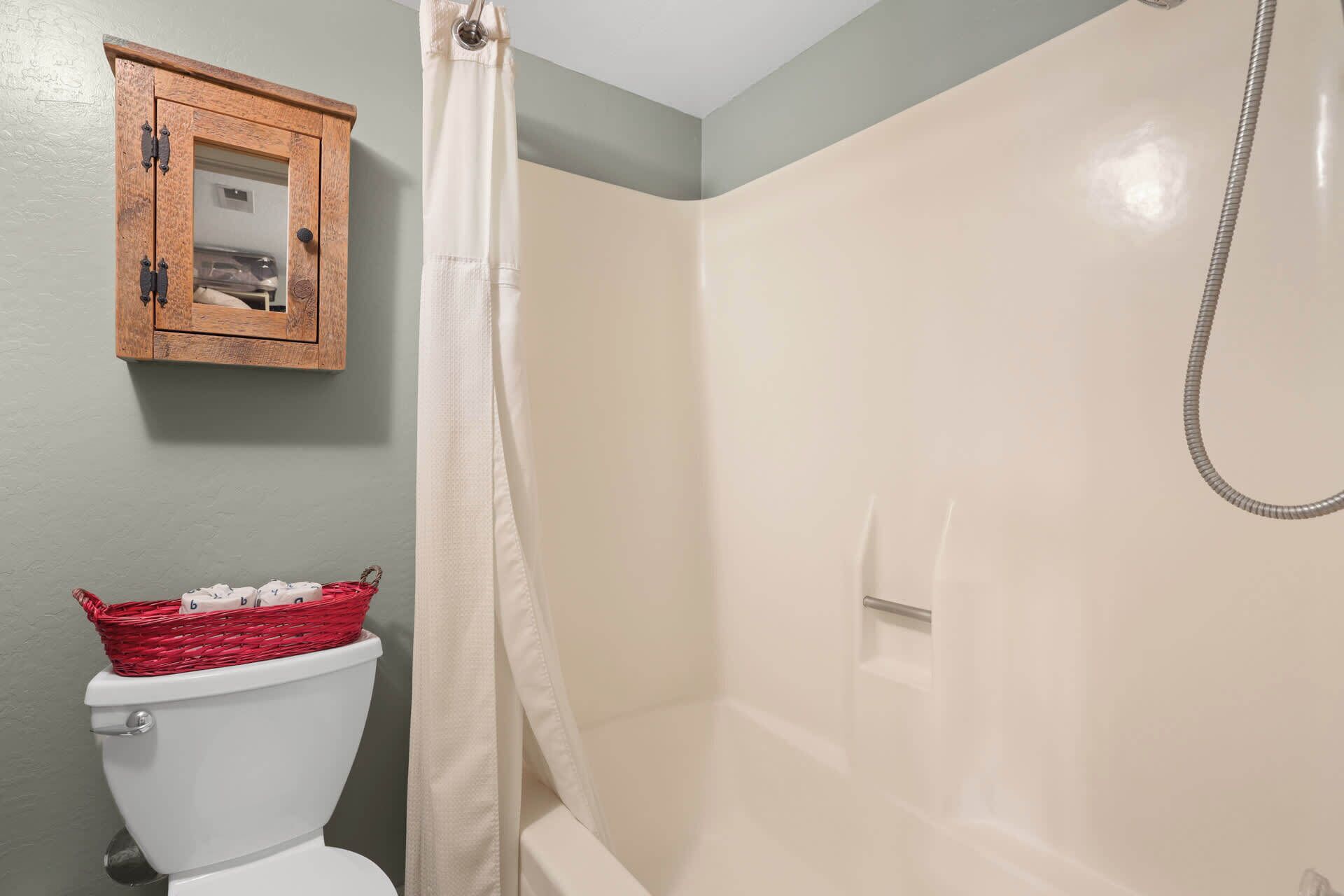 A bathroom with a white toilet, a wooden cabinet, and a shower area.