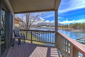 Terraza de madera con mobiliario exterior, con vista a un lago y montañas.