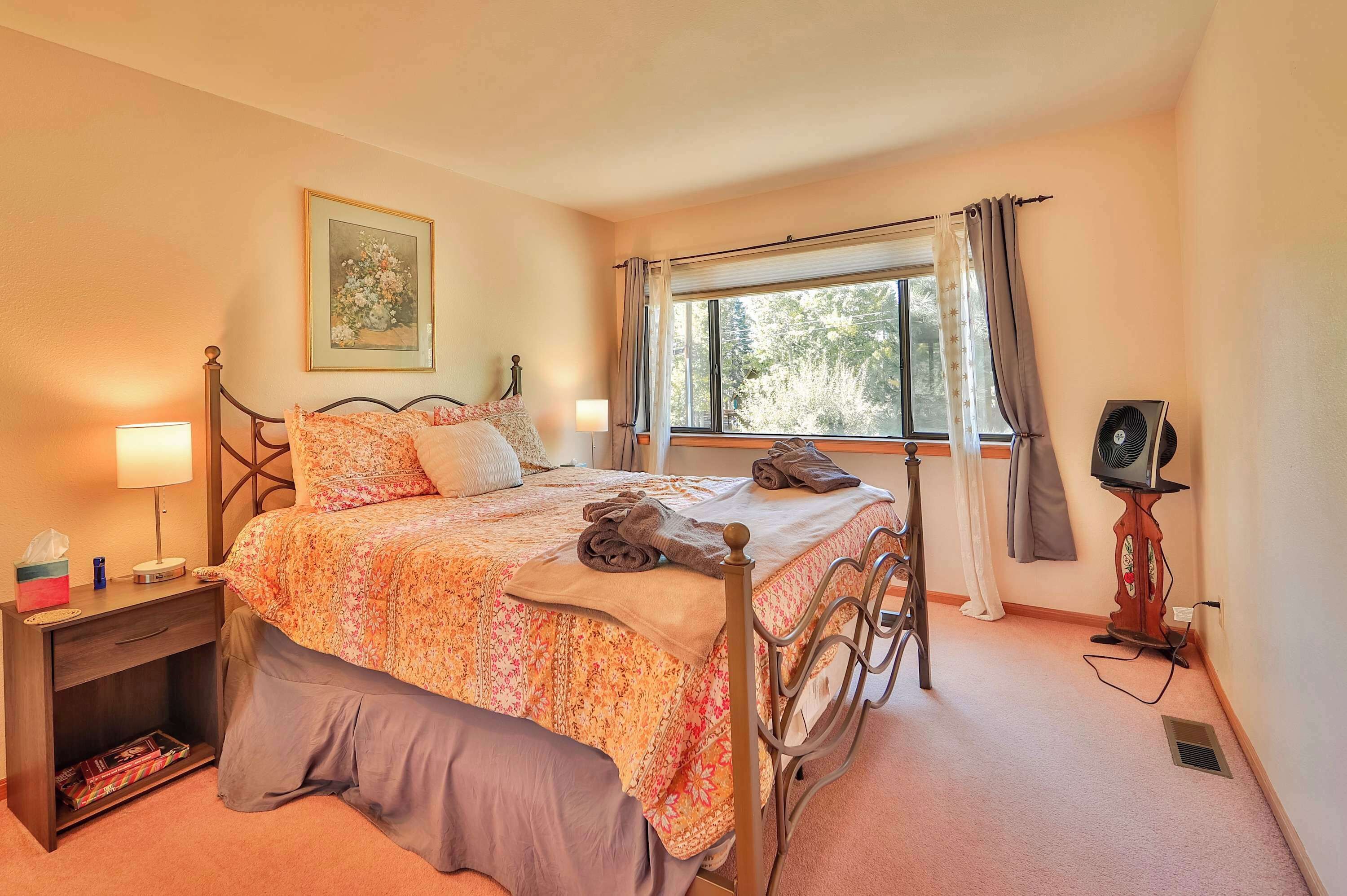A neatly made bed with a floral comforter, a bedside table with a lamp, and a window with curtains.
