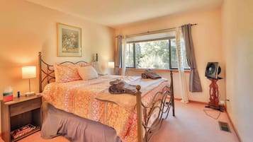 A neatly made bed with a floral comforter, a bedside table with a lamp, and a window with curtains.